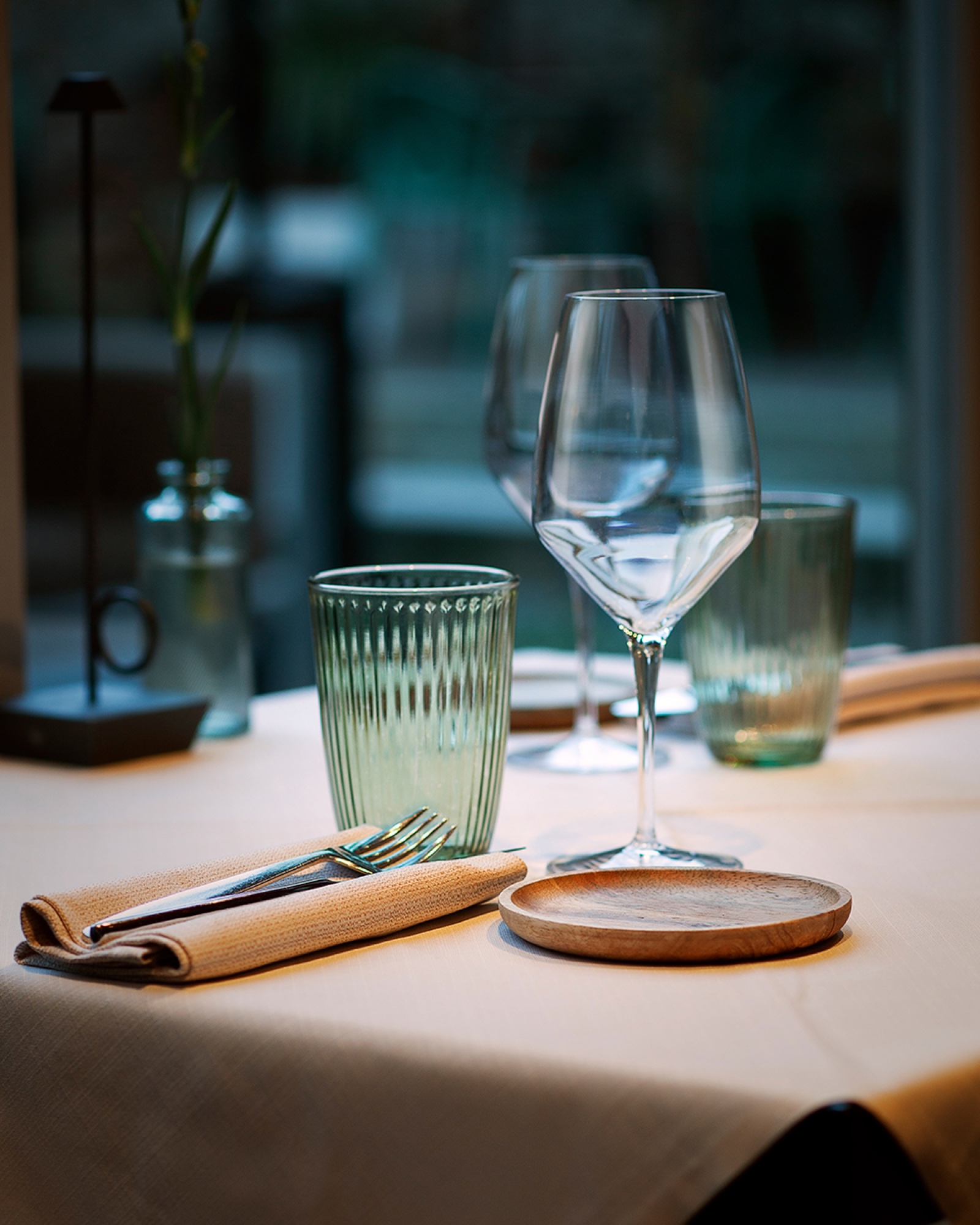 Mise en place del ristorante 19, con calici, bicchieri verdi e piattino in legno
